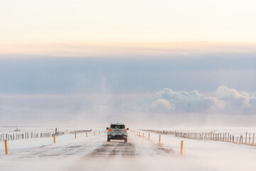 imagen de un coche conduciendo por una carretera nevada y nubes en el cielo azul 