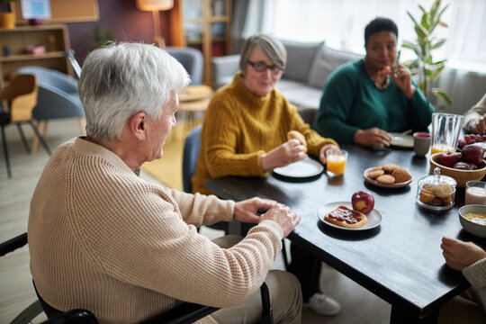 Side view portrait of senior man in wheelchair sitting at table in retirement home during breakfast - Powered by Adobe