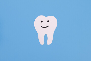 White paper smiling tooth on a blue background. Dental treatment, dentist services, oral care