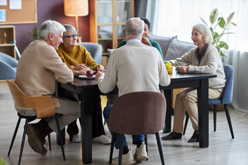 Group of seniors sitting at table together and smiling happily in retirement home common room