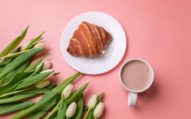 white tulips and croissant on a white plate on a pink background with space for text