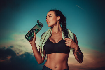 Young sports woman standing with bottle of water after training, tattoo on body