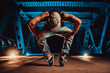 Young cool man break dancer posing on urban bridge at night, tattoo on body