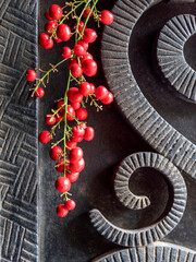 Black, rough forged iron surface with curved shaped decor and a bunch of bright red peppercorn fruits.