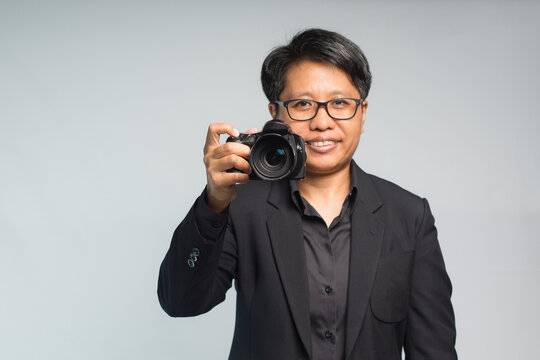 Photographer in a suit holding the digital camera while standing on a gray background