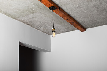 Loft style elements in the interior. Vintage incandescent light bulbs are spotted on wooden beams on a bare concrete ceiling.
