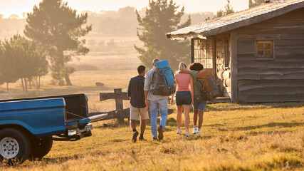 Group Of Friends Unloading Backpack From Pick Up Truck On Road Trip To Cabin In Countryside