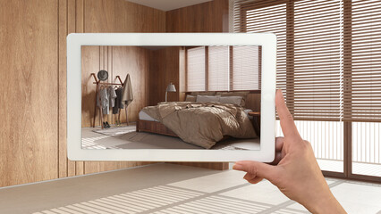 Obraz na płótnie Canvas Augmented reality concept. Hand holding tablet with AR application used to simulate furniture and design products in empty wooden interior with marble floor, farmhouse bedroom