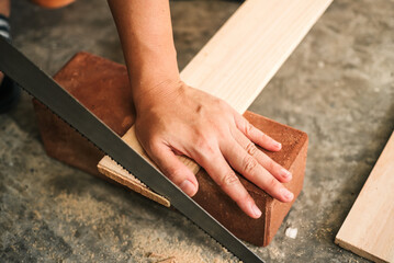 Close up carpenter craftsman using hand saw in workshop. Small business furniture industry.