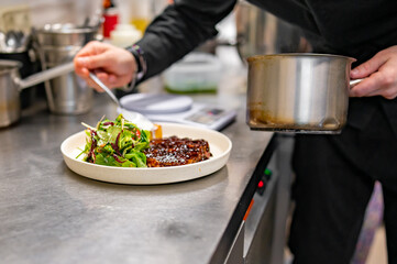 professional chef's hands cooking Grilled Ribeye Steak on plate with Potato gratin and salad in restaurant kitchen