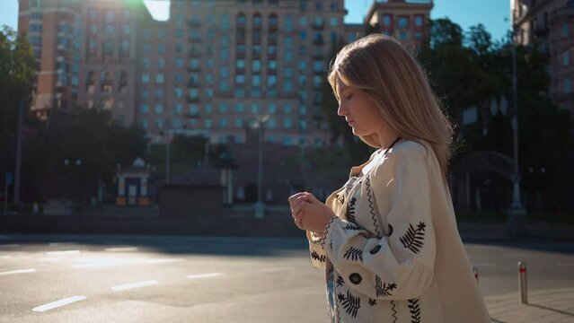 Side view thoughtful teenage girl standing on city street in Kiev Ukraine on the right. Medium shot beautiful teenager thinking waiting outdoors in the morning at sunrise. Slow motion