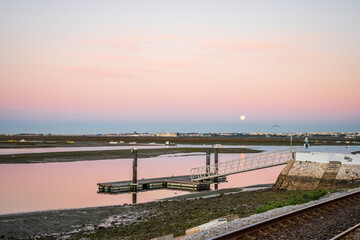 Fototapeta na wymiar Morning view of pier on Ria Formosa in Faro, with moon set shortly before sun rise, Algarve, Portugal