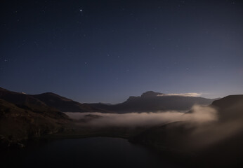 Night landscape in the mountains with rocky mountain ranges and night sky with stars, view from the cliff to the lake at night