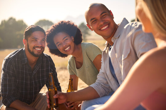 Group Of Friends On Vacation Sitting On Porch Of Countryside Cabin Drinking Beer Together