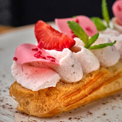 Eclairs with cream and strawberries on a white plate