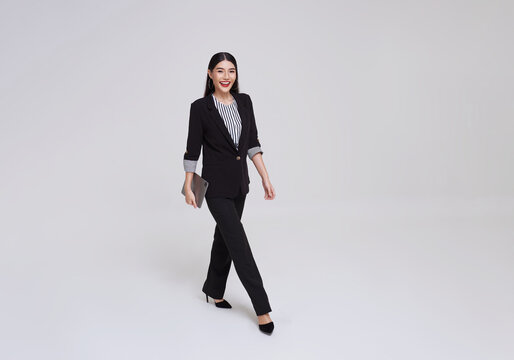Happy Asian business woman smile in formal suit holding tablet and walking over gray background.