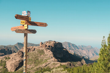 A wooden signage for travellers on a wild volcanic landscape with pine trees, cliffs and rock formations in Pico de las Nieves, Tejeda, Gran Canaria. Clear and sunny day