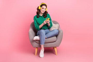 Full length photo of sweet shiny woman wear green shirt sitting couch enjoying songs modern gadget...