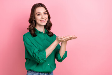 Fototapeta premium Portrait of optimistic satisfied girl with curly hairstyle wear green shirt demonstrate product empty space isolated on pink background