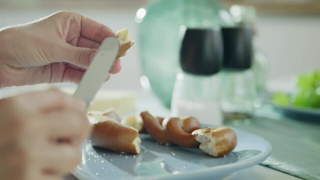 Closeup of someone spreading butter on a pretzel during breakfast