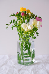Bouquet of spring freesia flowers in glass on white background