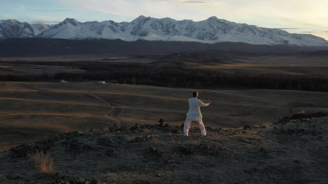 Video of wushu master in a white uniform training on the hill at sunset time.