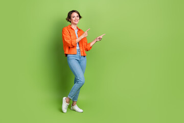 Full length photo of cute pretty woman wear denim jacket pointing two fingers empty space isolated green color background