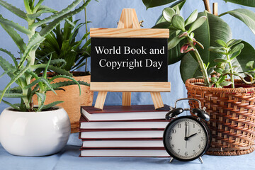 World Book and Copyright Day written on black board on stack of books on blue background with...