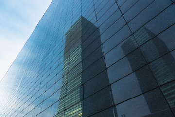 The skyscraper is reflected in the windows of the facade of a modern glass building
