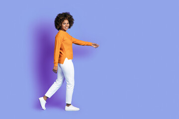 Fototapeta na wymiar Cheerful stylish curly black woman walking towards copy space