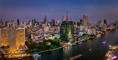 Panoramic view of the illuminated skyline of Bangkok, Bang Rak and Sathon district, Thailand, along the Chao Phraya river during dusk