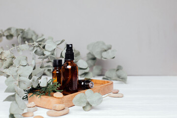 Amber bottles with facial cosmetics with a branch of eucalyptus on the white wooden background, facial cleaner, serum. Front view