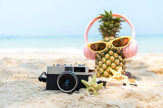 Select focus. Summer in the party.  Hipster Pineapple Fashion in sunglass and listen music with vintage camera on the sand beach beautiful blue sky background.  Fashion Summer Vacation Concept