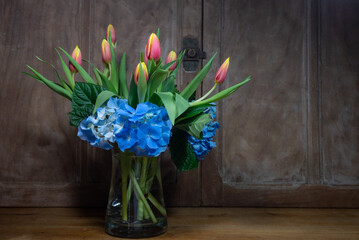 bouquet tulipes et hortensia vase transparent devant portes anciennes