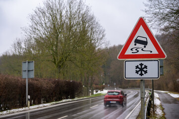 Car passing on a wet road in winter with a slippery road and ice warning sign