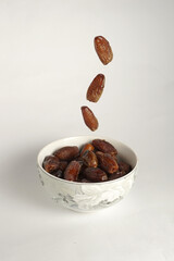 some dates fall into a bowl of dates with a plain white background