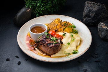 Dinner filet mignon beef steak with mashed potatoes, corn, tomatoes and sauce.