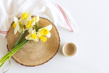 Closeup beautiful white daffodils on a brown wooden board. Spring flowers. Spring background. Cup of coffee with milk. Breakfast composition, Easter.
