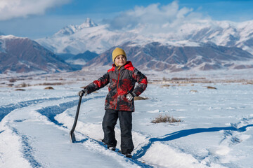 Fototapeta na wymiar Child with shovel standing on winter mountains background