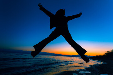 Man jumping on lake background silhouette at sunset light