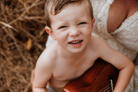 Young boy sitting on mother's lap in long grass, smiling up at camera