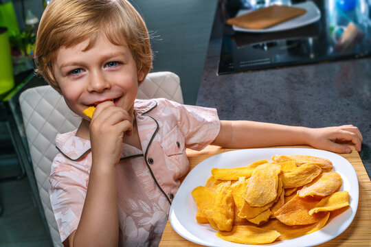 Smiling Child Eating Dried Mango On Kitchen