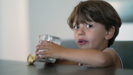 One candid small boy drinking milk. Thirsty Child holding glass drinks nutritious food