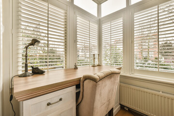 a window with shutters on the outside and an office desk in the middle part of the room is empty