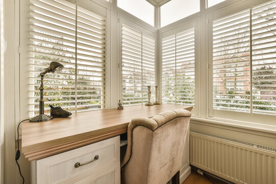 a window with shutters on the outside and an office desk in the middle part of the room is empty