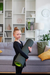 Child holding fitness mat in room. Physical exercises for children at home. Concept of sport