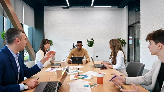 Multiracial group of people at business meeting in an office, discussing business affairs with each other, papers and gadgets on the table