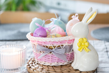 Easter decoration of colorful eggs in a basket and a rabbit on the kitchen table in a rustic style. Festive interior of a country house