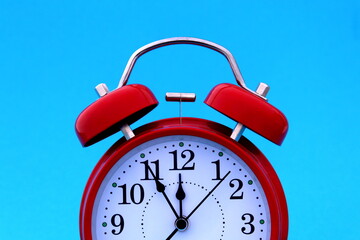 A red alarm clock stands on a blue background. The time shows five minutes to twelve