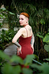 redhead beautiful woman with green eyes  and short hair and tattoo in brown dress with palm leaves in the jungle